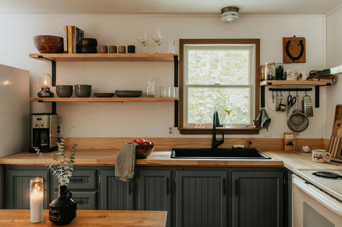 A kitchen with wooden shelves containing bowls and cups. A candle is lit on the island bench with a fruit bowl in the background. 