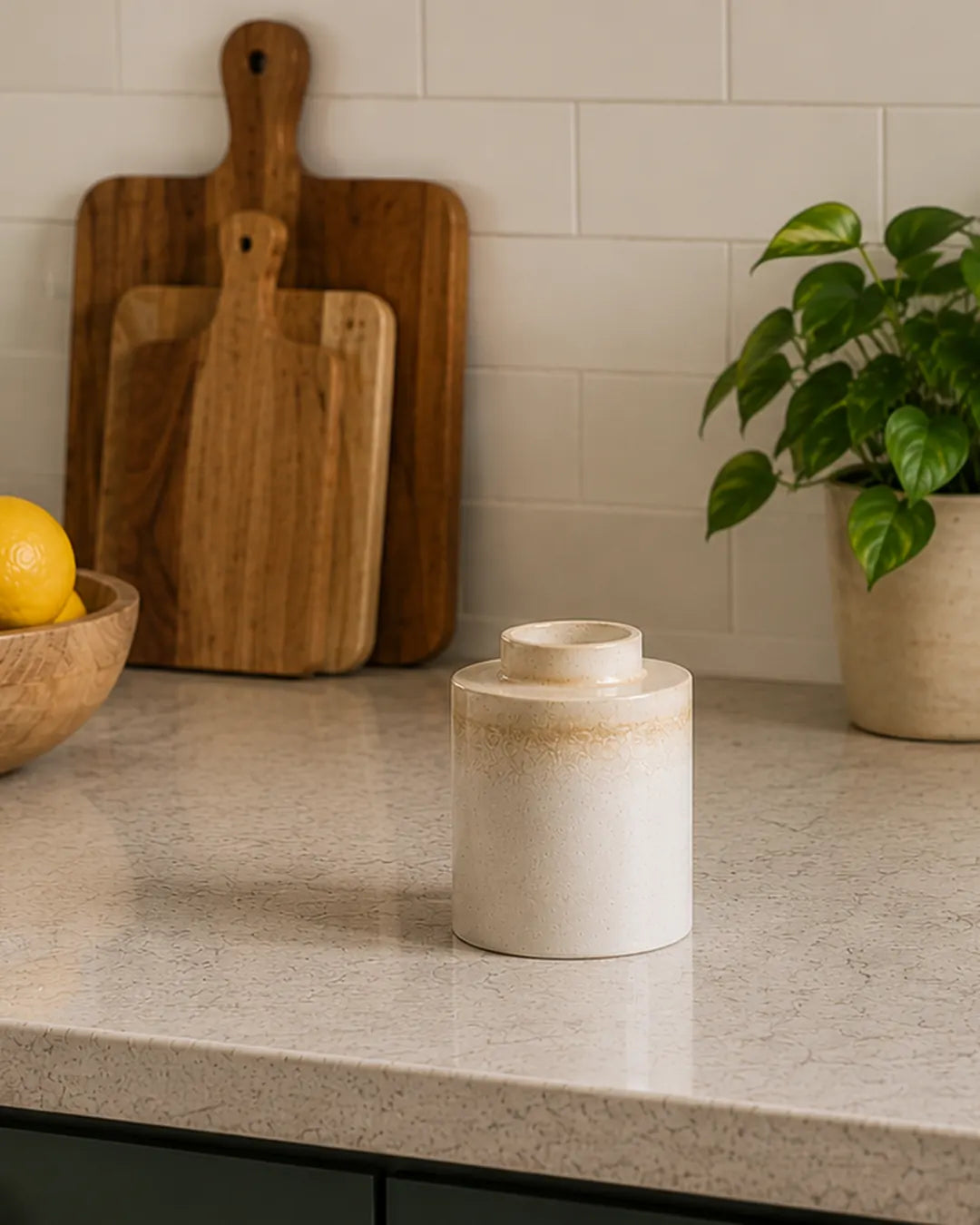 White ceramic jar on a kitchen counter with wooden cutting boards and a plant in the background.